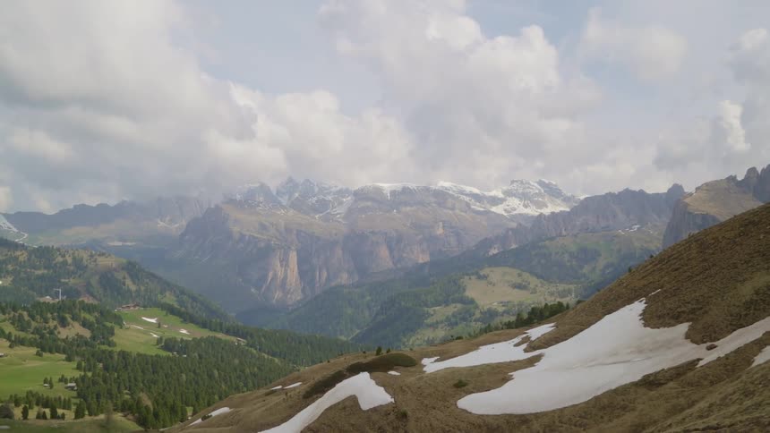 Melting snow is on the hillside with mountains in the distance under a cloudy sky