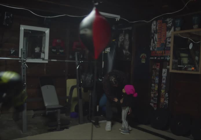 Black girl at the gym punching a small bag with a father holding his child daughter on his arms in the background