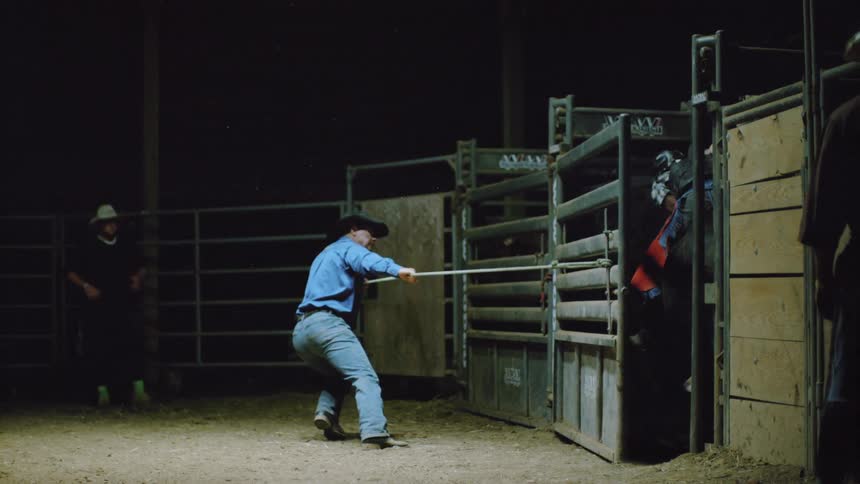 A man opens a gate for a bull rider to charge out