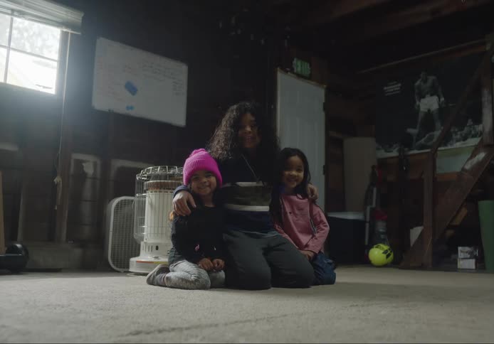 A woman is kneeling on the floor with her arms around her two little girls as they smile