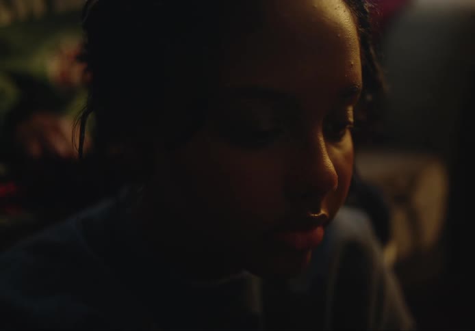 Black teenager girl sitting down while an adult woman braids her hair indoors