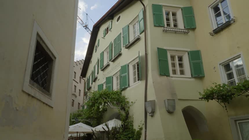 A yellow residential building with green shutters on the window in an area with other buildings near by