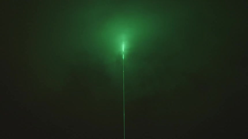 Strong green laser light pointed into the sky at night with clouds and clear weather