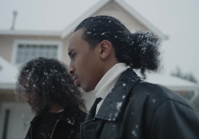 Two men stand in front of house shivering in the falling snow