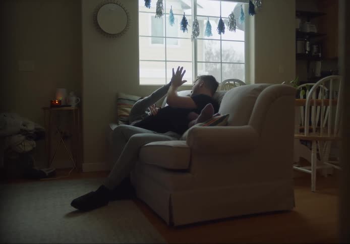 A couple playfully holding hands and touching while on the love seat at home