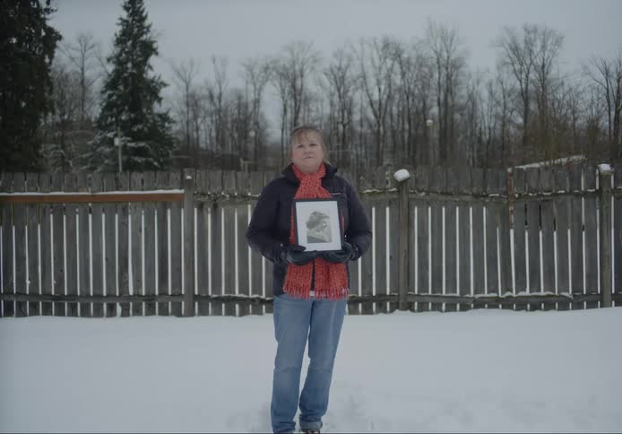 Woman poses holding portrait midtorso near fence in winter