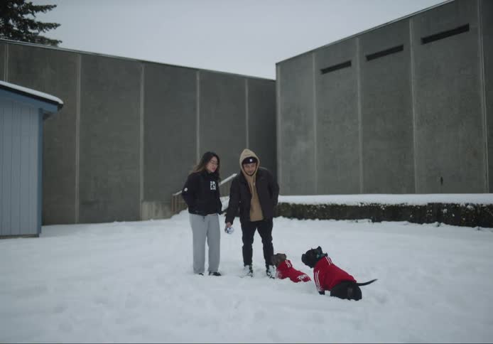 Man and woman playing with their dogs holding a small ball in the midst of winter with snowcovered ground