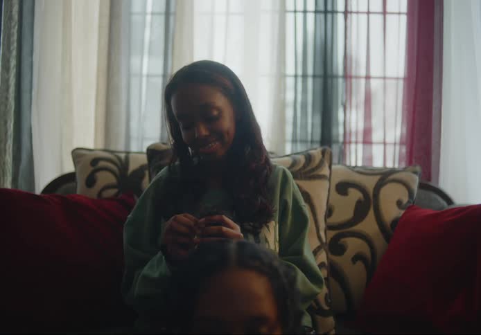 Black woman sits on sofa and braids friends hair