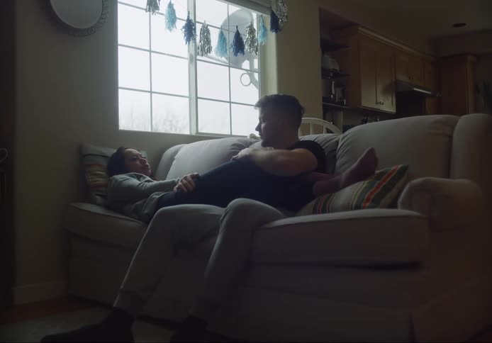 A man and a woman are sitting on the sofa cuddling with their hands