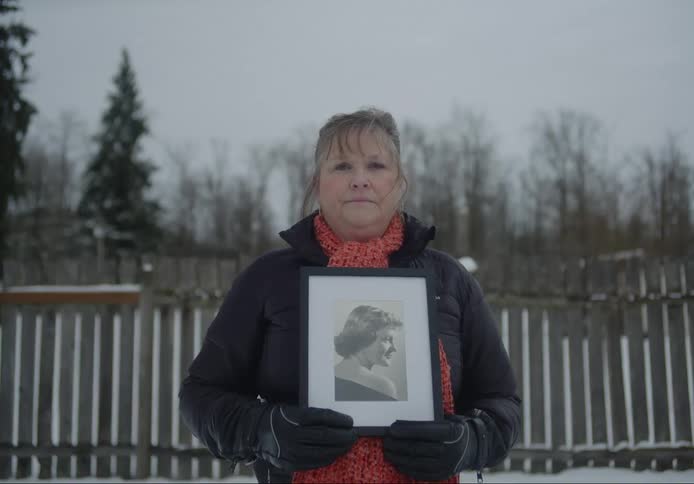 Woman wearing winter jacket and gloves holds 8x10 framed portrait