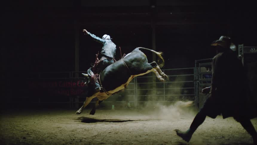 A man is riding a bull in a dark arena