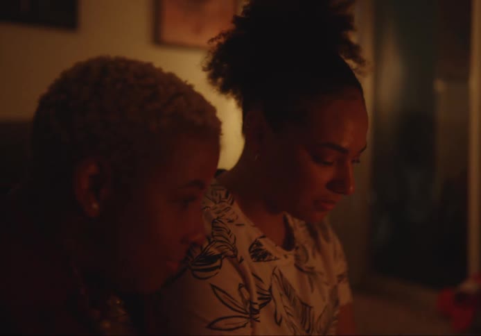 Two women are sitting in the living room together as one woman drinks a cup of coffee and the light from the fireplace shines on their faces