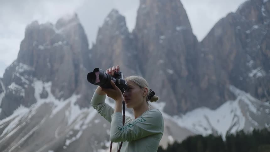 Woman photographing with a professional camera in a natural environment with trees and snowcovered mountain range