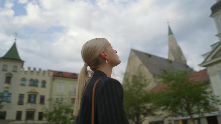 Woman in the center of a square observing the architecture and facing a church