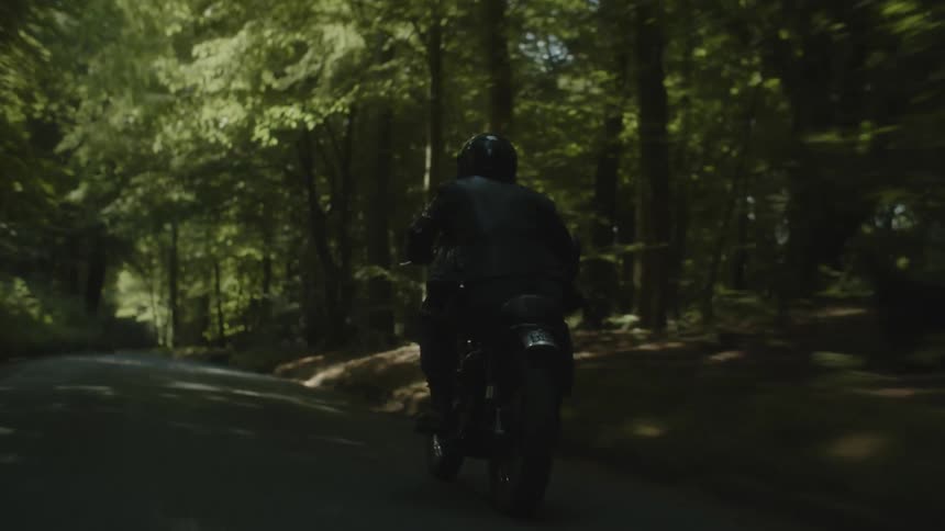 Person riding a motorcycle on a road in the midst of nature surrounded by trees