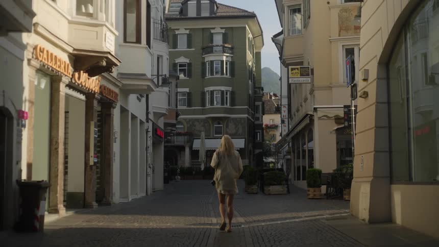 A blonde woman walking down a street in the middle of the city with several buildings of ancient architecture