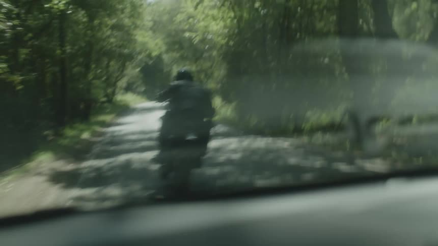A biker in a jacket and black helmet on a street in the middle of the forest