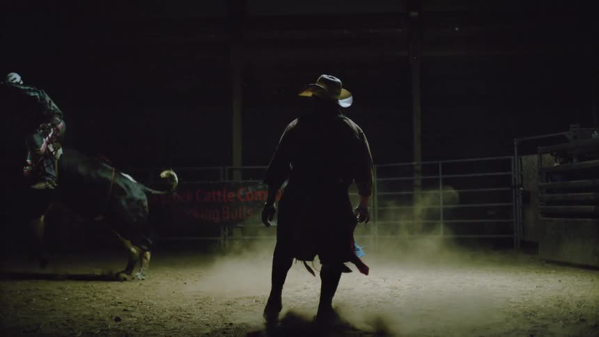 A man is riding a bull as another stands by
