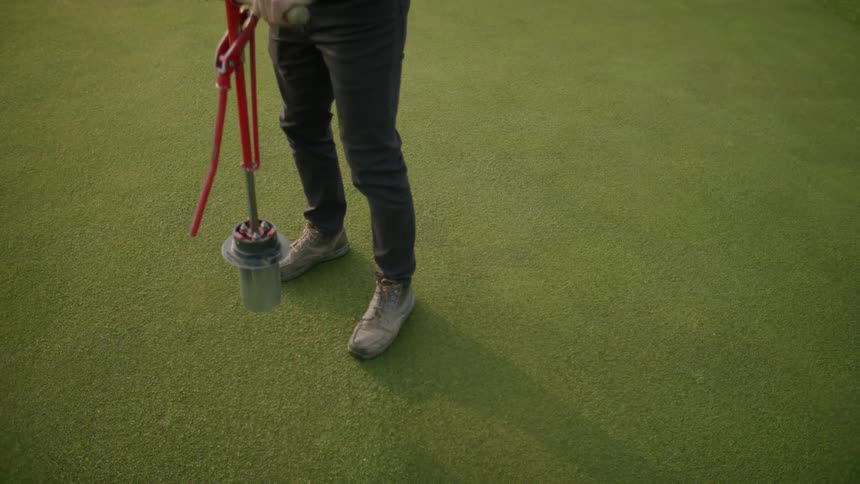 Man using a manual machine to dig a hole in the golf course turf