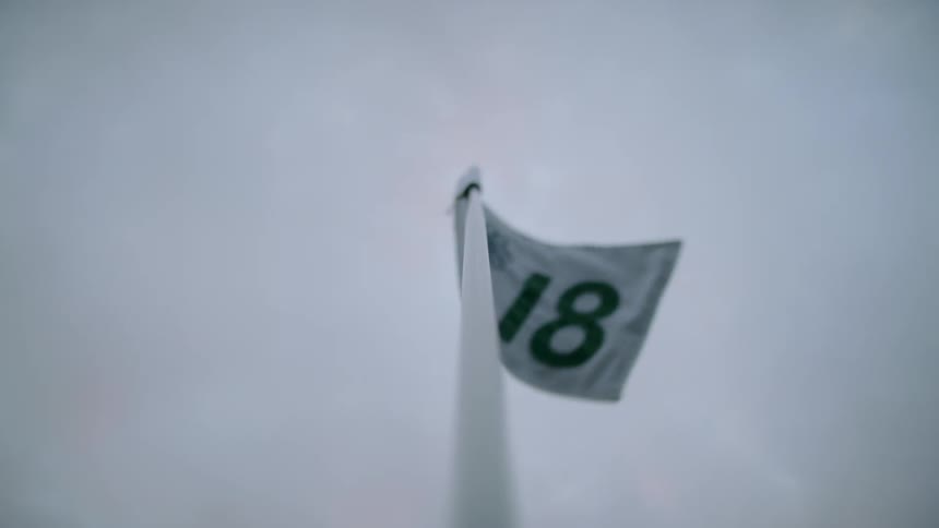 Flag at the eighteenth golf hole flaps in the breeze on an overcast day