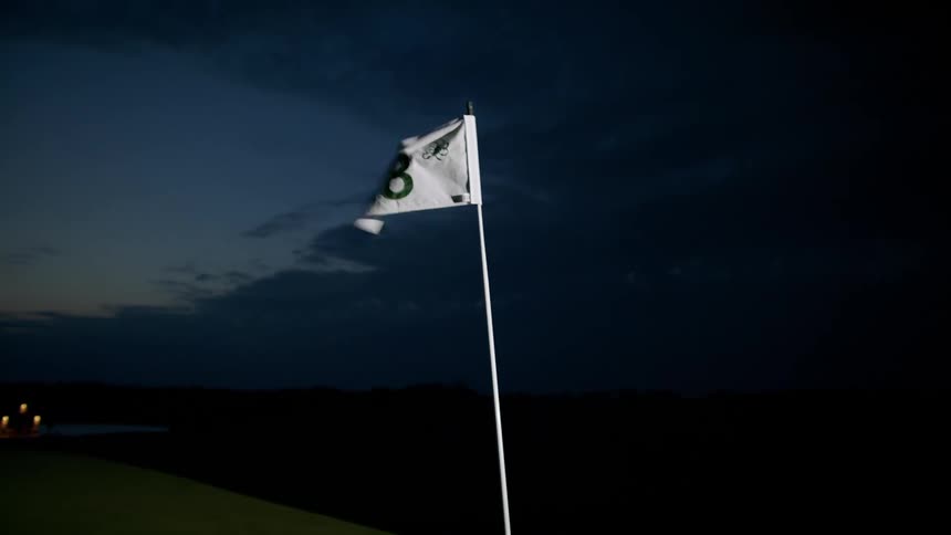 Flag at eighteenth hole of golf course flaps in wind at night