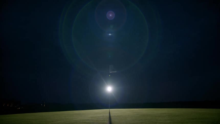 The flag on the flagstick flaps in the wind on a golf course at night