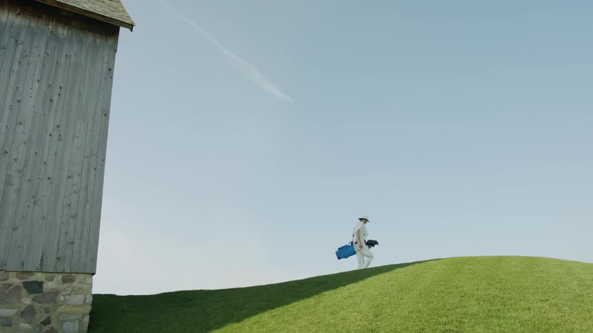 Man carrying a backpack on his shoulder walking on a uneven grassy terrain