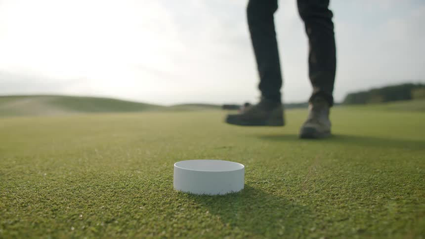 A man walks toward a golf hole and pushes a white insert into place then walks away