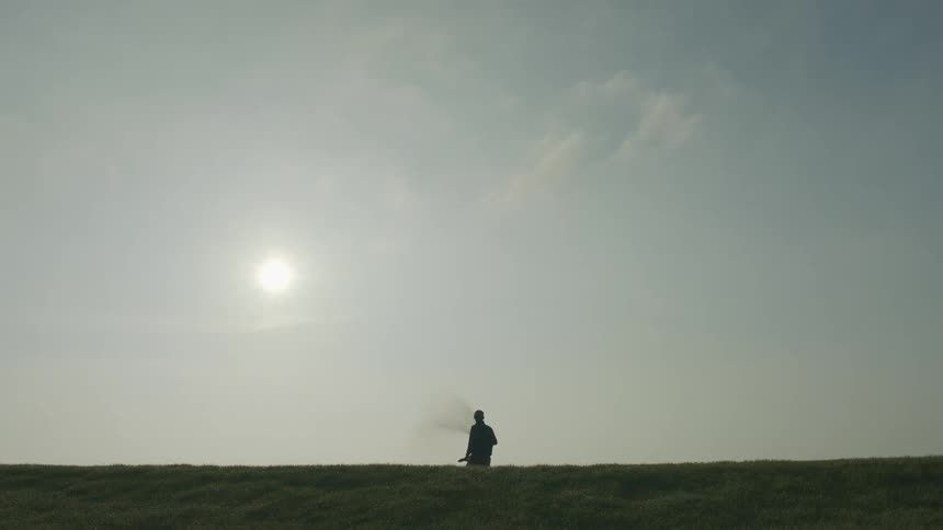 Man facing away from the camera outdoors in a grassy area watering the surroundings with water