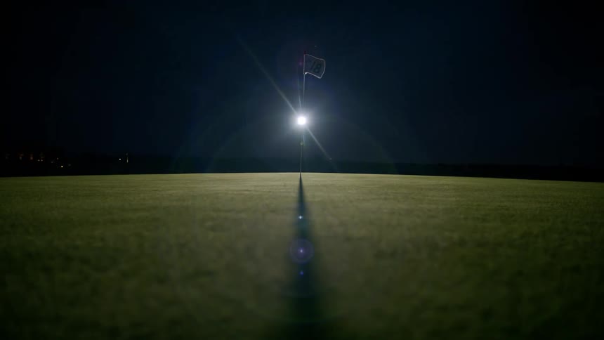 A flag planted in a lawn moving with the wind and in the background a flare of light