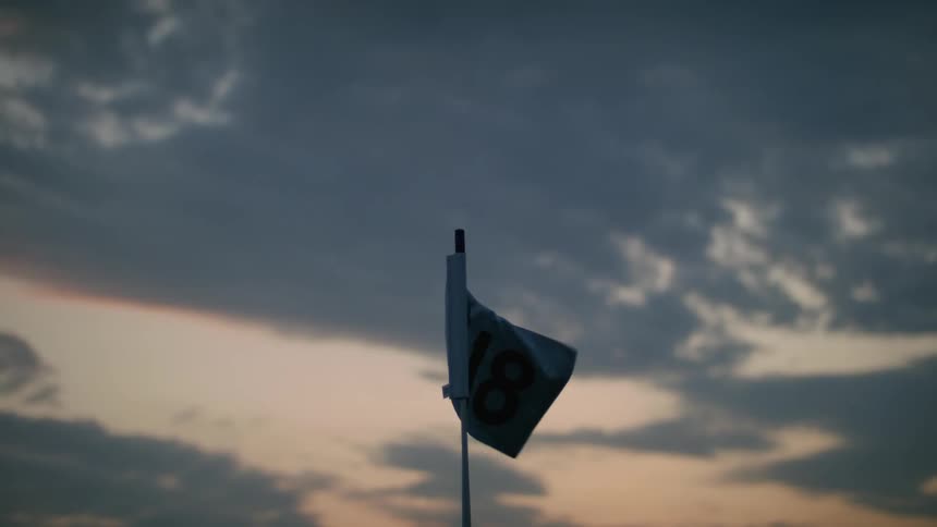 Golf flag flaps in breeze under red tinted sky on a cloudy day