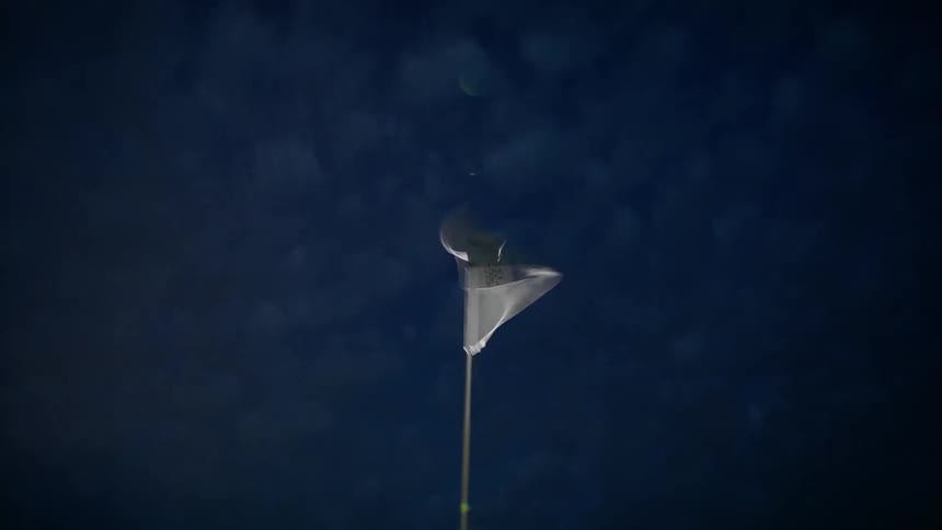 The flag on the flagstick flaps in the wind on a golf course at night