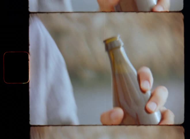 Dynamic handheld 8mm film clip of a man that pops the top or crown cap off a brown glass bottle using a bottle opener and opens and drinks beer to enjoy a cold and refreshing beverage on a warm summer or spring time day