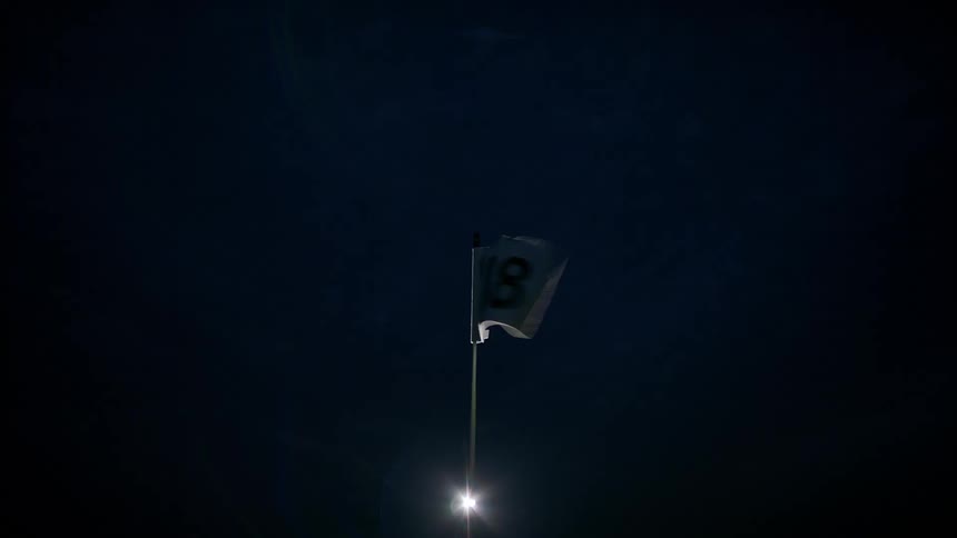 The flag on the flagstick flaps in the wind on a golf course at night
