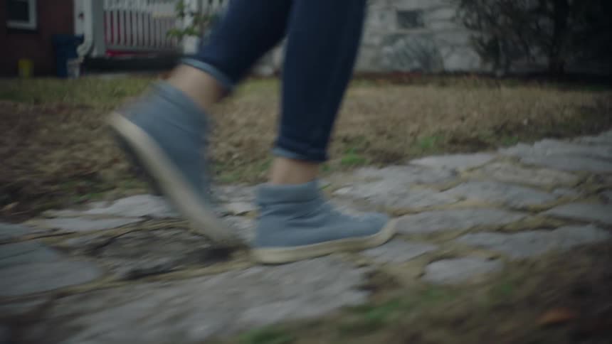 Closeup of a persons legs walking on a sidewalk towards a residence