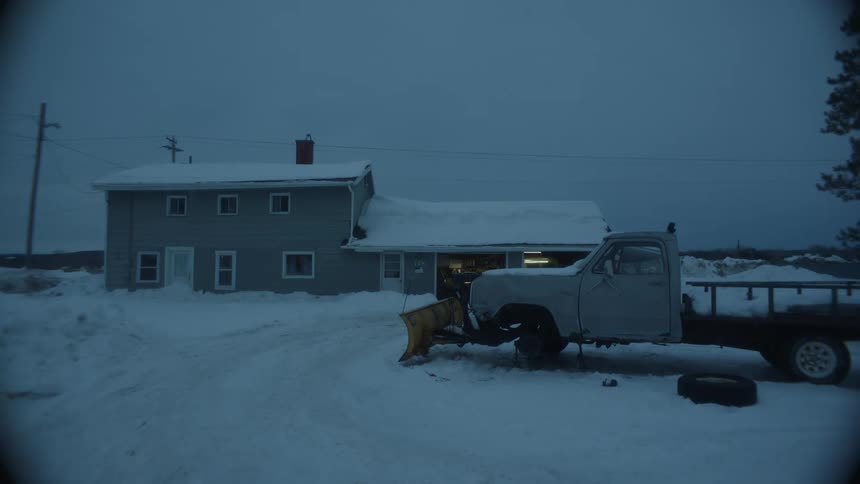Truck parked in front of a residence without its front wheels and the ground covered in snow