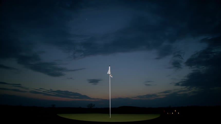 A flag with the number 18 stamped on it is planted on a golf course and is moving with the wind