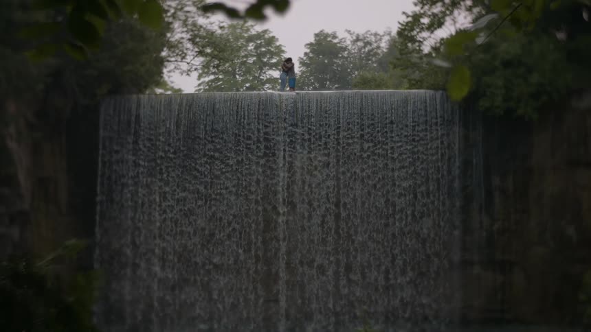 Couple stands in embrace atop waterfall