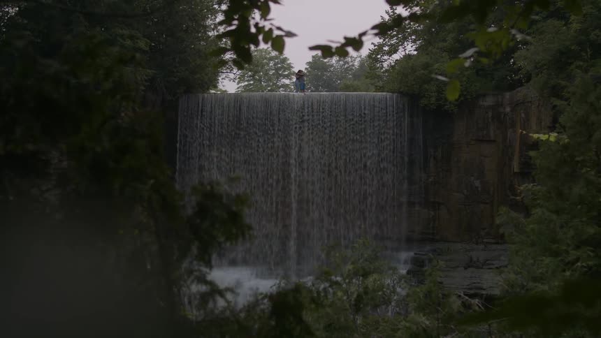 Two people crossing a river next to a waterfall and meeting half way for a hug during day time