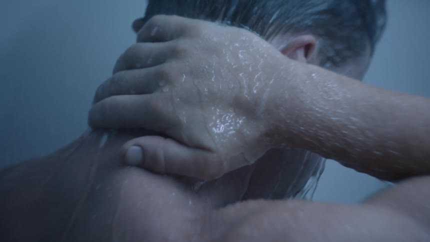 Shower water splashes on a man as he moves his hand down the back of his neck