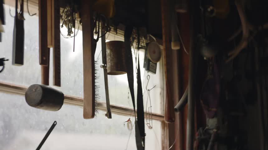 A brush and tools hanging from the ceiling near a window are swaying as they move
