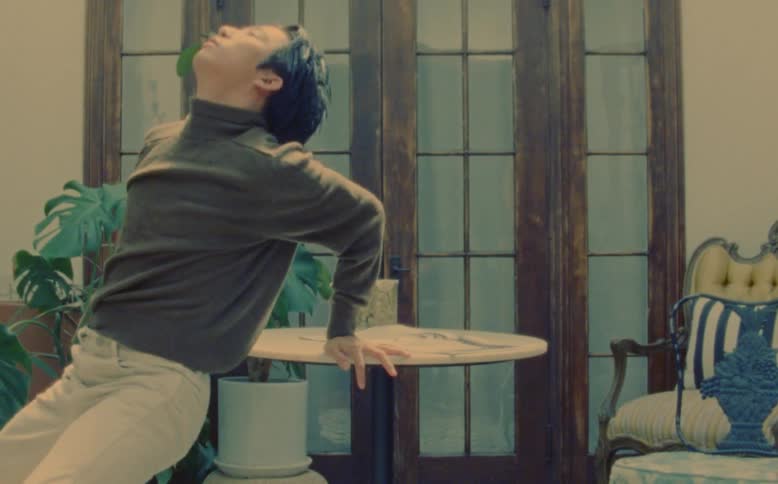 Asian man outdoors on a porch next to a table dancing and then sipping from a cup during day time