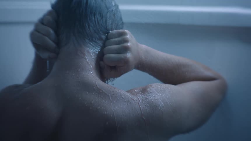 A man holds his hands to his head as he stands in the shower