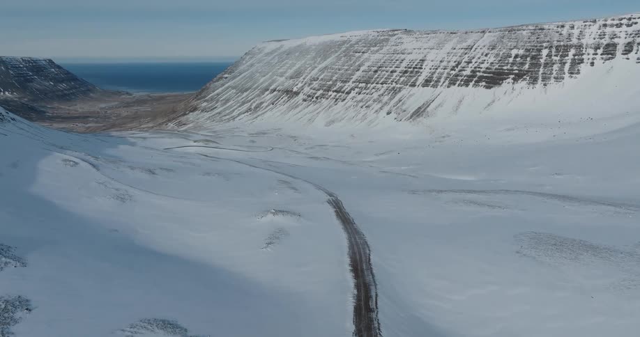 Aerial of a road through a snow covered valley in the mountains next to the ocean