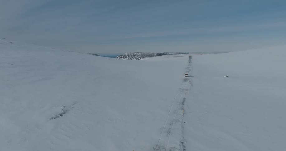 Terrain that is covered in snow has a lone line of vehicle tracks carved into it