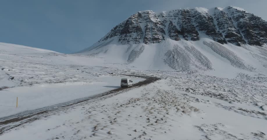 A white van travels on a road toward a mountain on a snow covered winter day under a clear blue sky