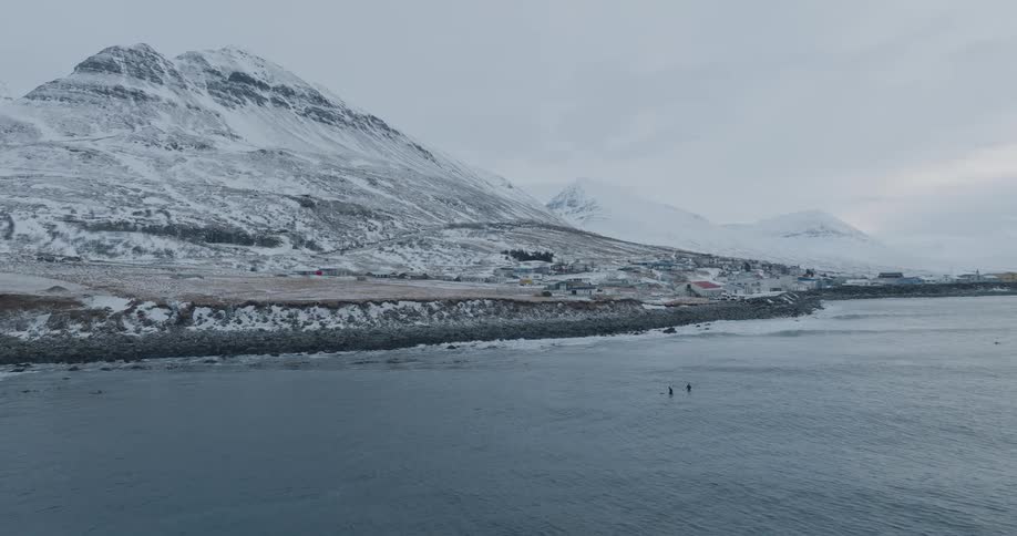 Two surfers in the ocean with snowcovered mountains in the background