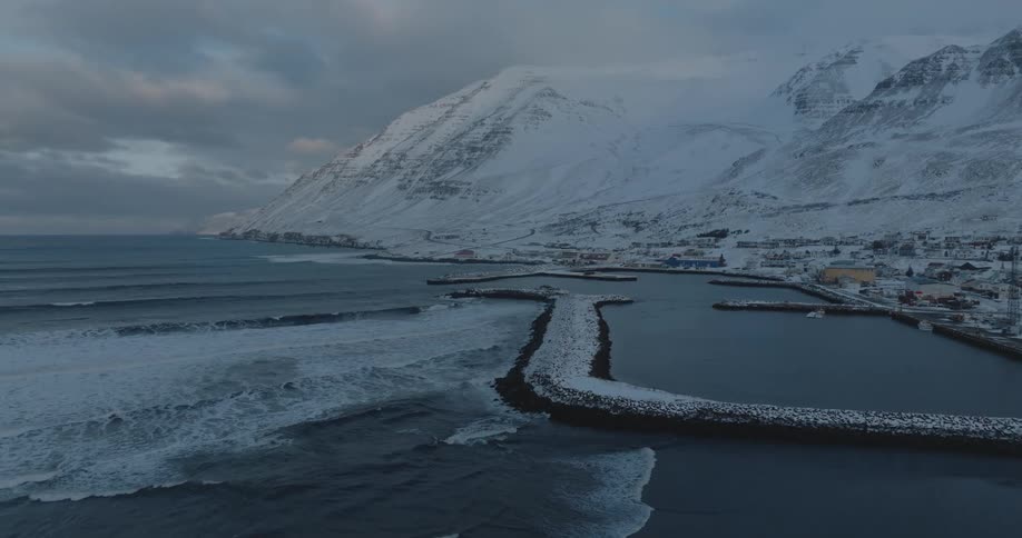 Aerial of a coastal town next to the snowcovered mountains at evening
