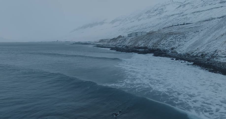 View of the sea with a surfer paddling and snowcovered mountains in the background