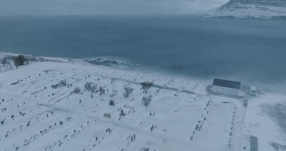 A small house in a snow covered field on the edge of an ocean